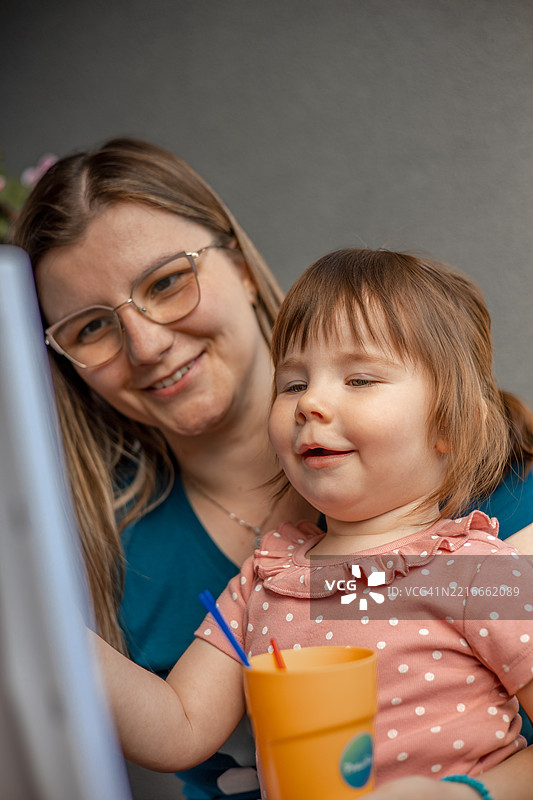 一个小女孩在母亲的温柔指导下，使用水彩颜料和画笔在画布上创作自己的杰作。图片素材