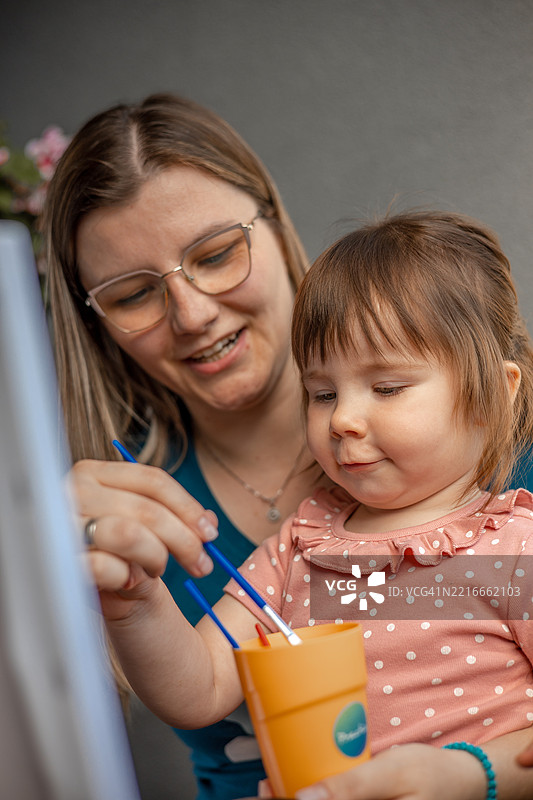 一个小女孩快乐地在画布上作画，身边有她的母亲，捕捉到了一幅美丽的创造力、亲情和艺术表达的瞬间。图片素材