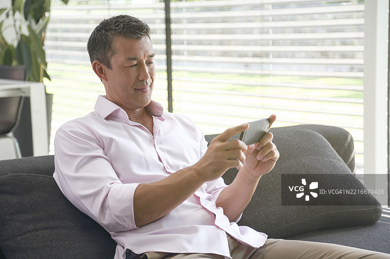 在家沙发上享受智能手机内容的未婚男子图片素材