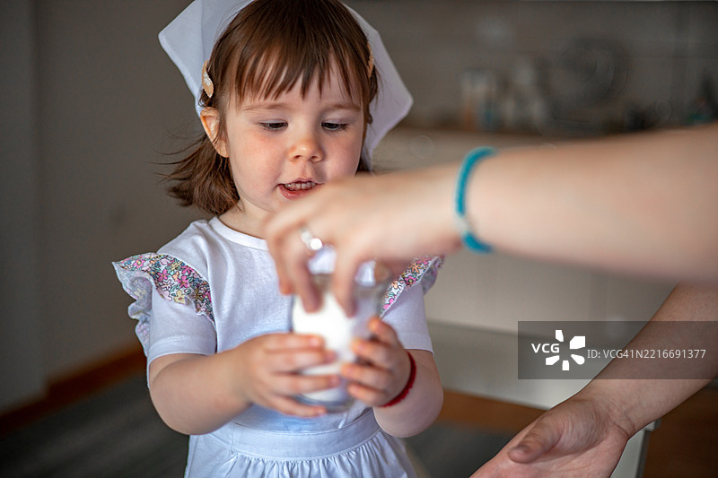 小女孩在厨房里拿起一杯酸奶作为早餐，愉快地开始新的一天。图片素材