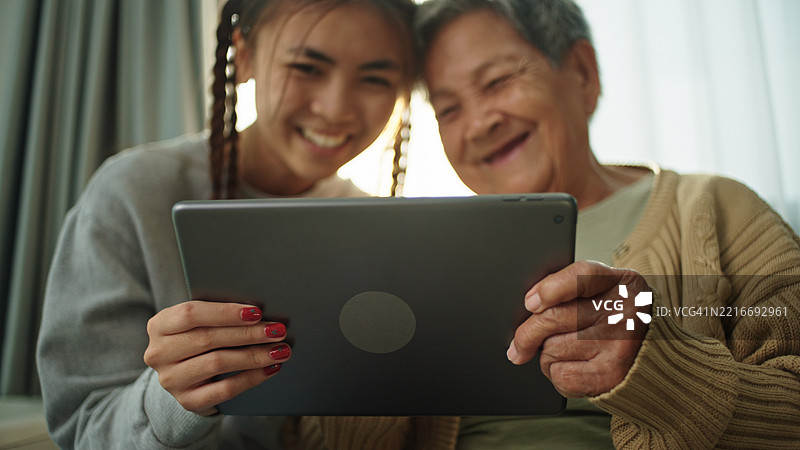 老年人与青少年一起在数字平板上玩游戏。图片素材
