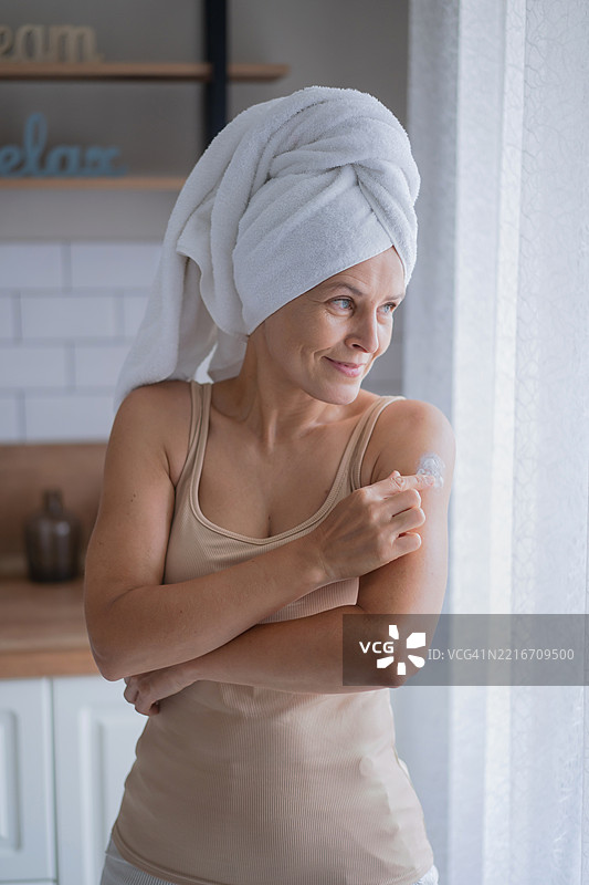 年轻女性在明亮的房间里给手臂涂抹护肤霜图片素材