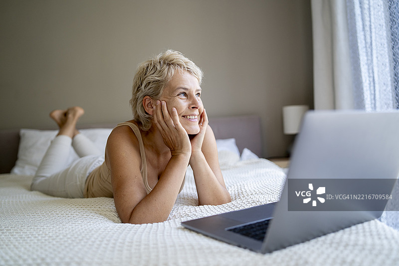 一位快乐的女性躺在床上使用笔记本电脑工作图片素材