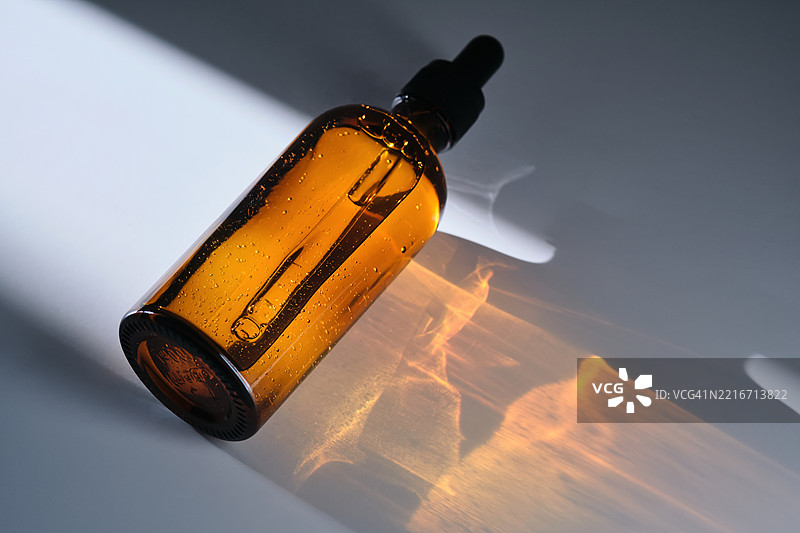 一瓶棕色玻璃制成的精华液，背景为白色，带有光线条纹。图片素材