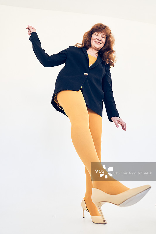 一位年长的女性单腿站立在白色背景上。平衡概念。图片素材