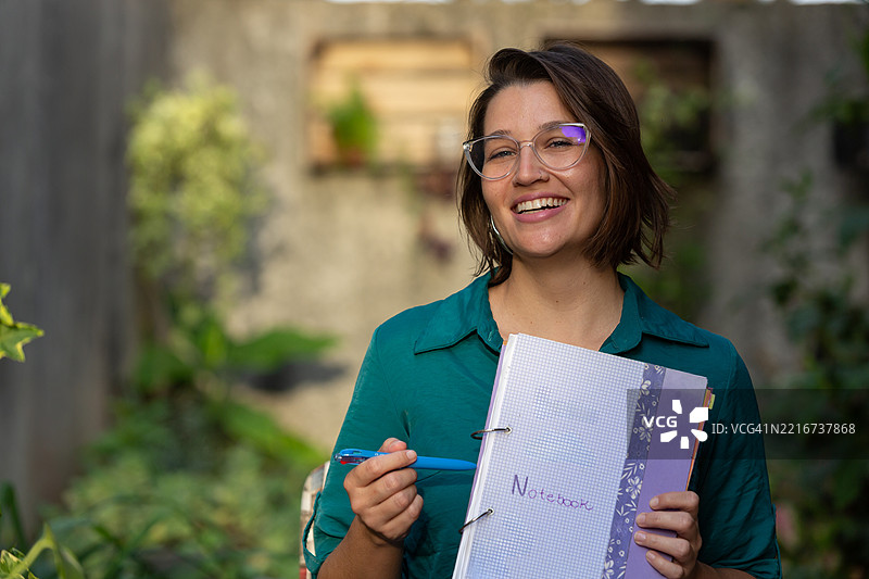 在后院微笑的白人女性手持笔记本的肖像图片素材
