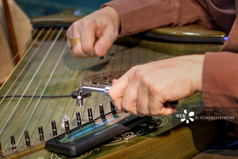 男子用调音工具和智能手机应用调音的传统弦乐器特写镜头图片素材