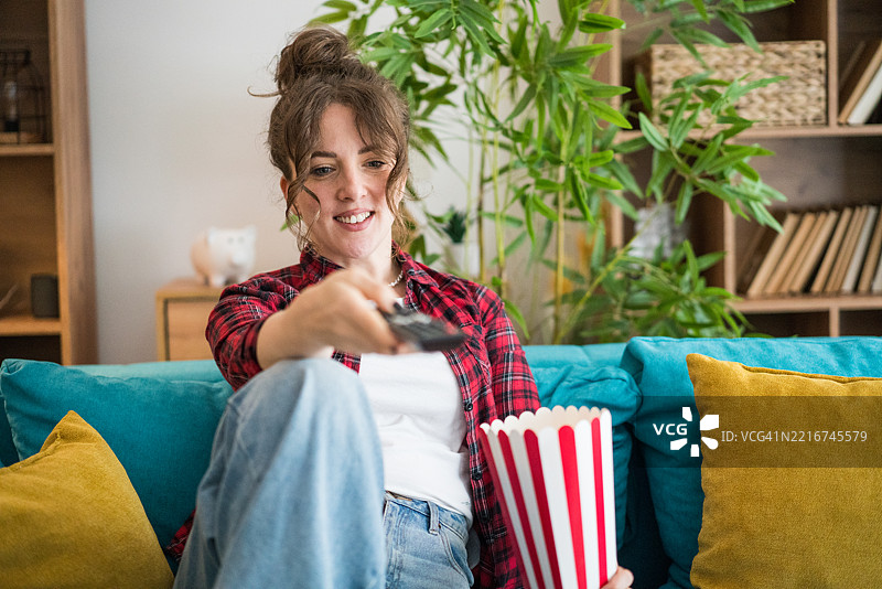 年轻女性在家沙发上看电视吃爆米花图片素材