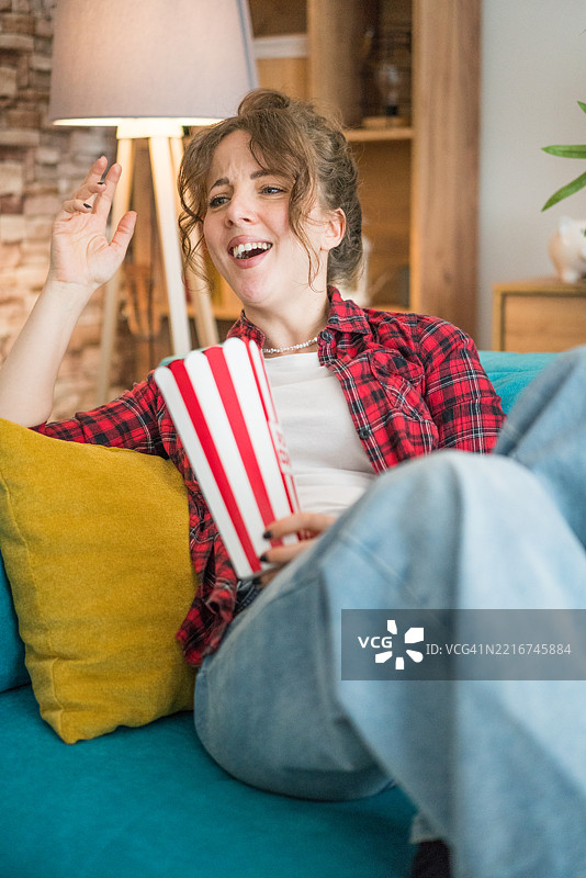 年轻女性坐在沙发上看电影，吃着爆米花图片素材