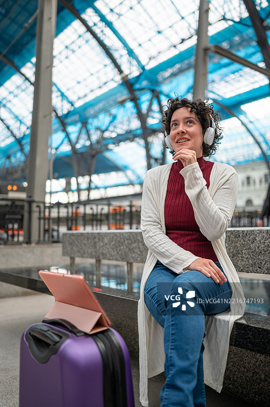 游客坐在火车站的长椅上听音乐，等待火车。图片素材