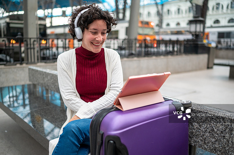 旅游女性在等火车时，戴着耳机听音乐并观看平板电脑。图片素材
