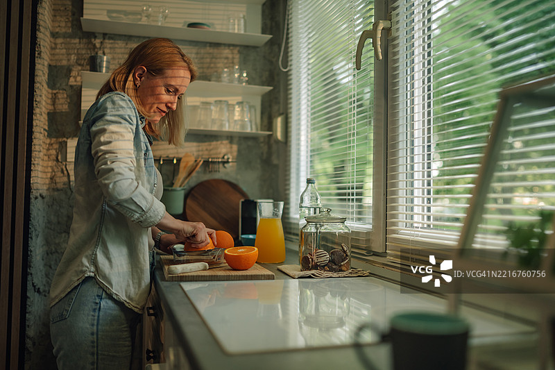 现代厨房中，女人在自然光下剥橙子图片素材