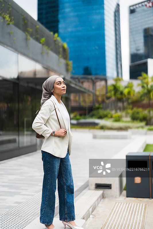 现代高管背着背包，站在城市建筑背景前。图片素材
