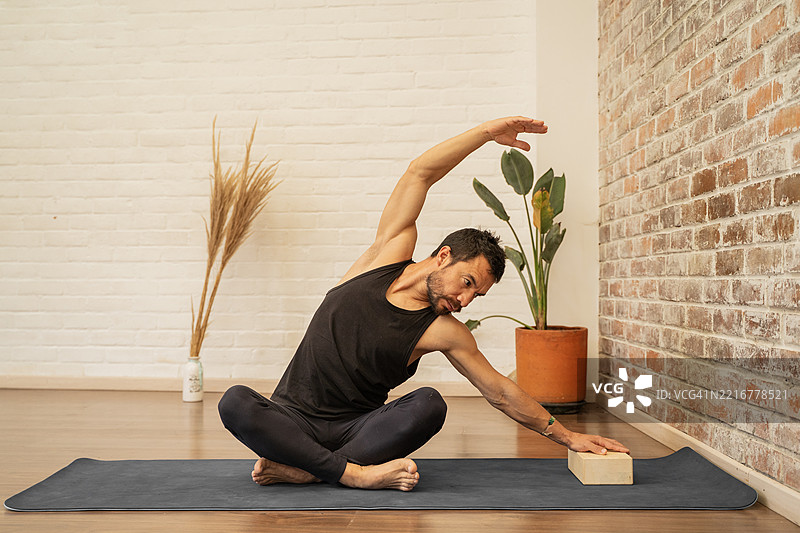 男子使用瑜伽砖练习坐姿侧伸展图片素材