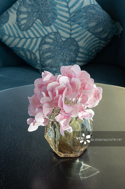 一瓶花放在黑色桌子上，背景是蓝色叶子图案的抱枕。图片素材