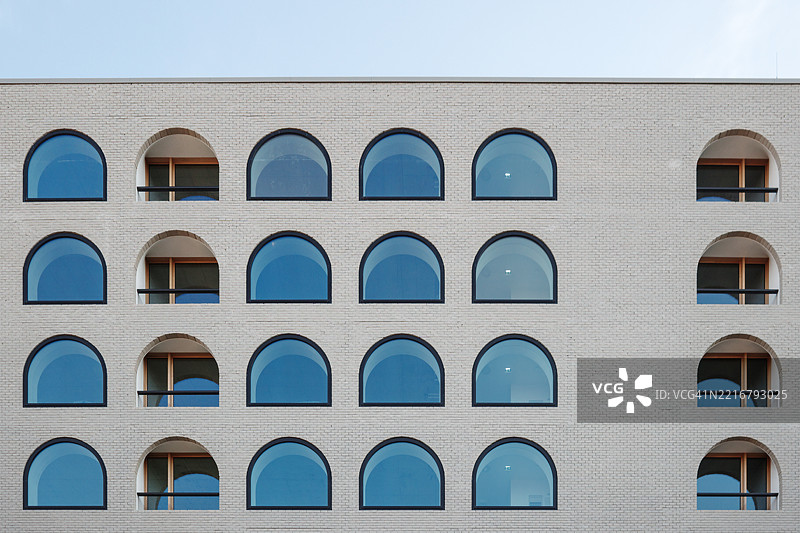 建筑立面具有均匀间隔的拱形窗户网格，配有反射蓝色玻璃。图片素材