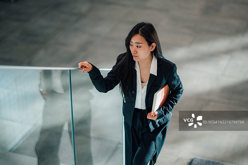 女商人在现代办公大楼的楼梯上走下。图片素材