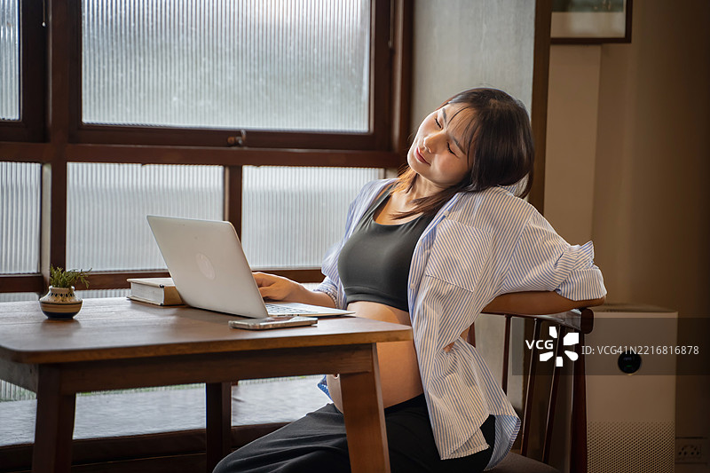 亚洲孕妇因在家办公时坐在桌子前使用电脑而感到背部疼痛。图片素材