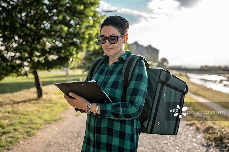 背包送货员在阳光明媚的户外散步时查看文件图片素材