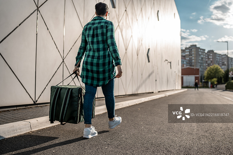 在城市环境中走在人行道上的人，手里提着一个包图片素材