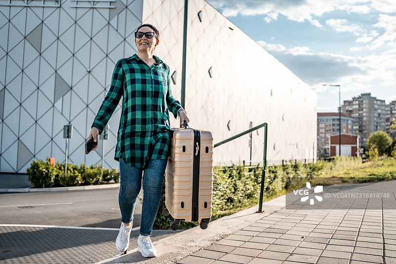 微笑的旅行者在阳光明媚的户外提着行李图片素材