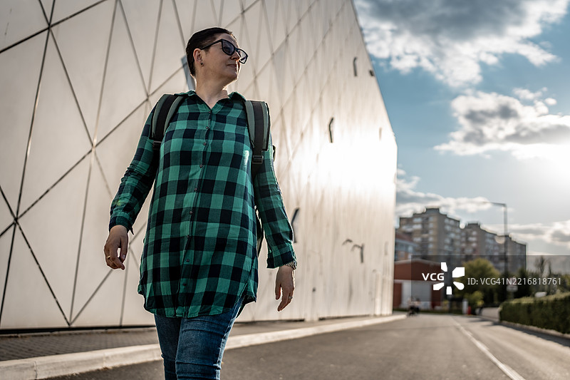 在阳光明媚的城市区域，时尚现代建筑背景下的女性步行图片素材