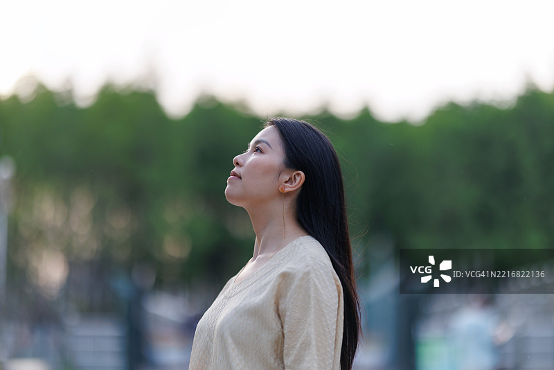 美丽的年轻亚洲女性在大自然中闭眼冥想，感受自由与放松。享受新鲜空气，仰头呼吸宁静。与自然的自由连接。健康与幸福的概念。图片素材