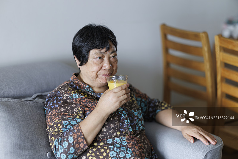 一位退休的亚洲老年女性正在喝橙汁以补充维生素C。图片素材