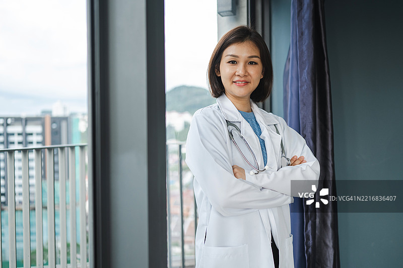年轻亚洲女医生穿着白大褂，面向镜头，站在医院内。医院或诊所的医疗系统为患者提供服务。图片素材
