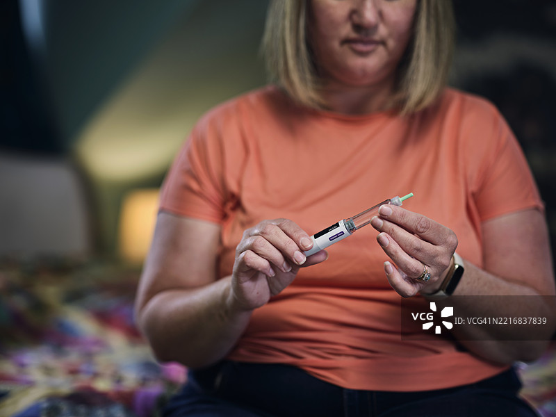 一位女性在家中准备她的减肥注射剂量，使用的药物是可以装载Saxenda（利拉鲁肽）或Wegovy（塞马格鲁肽）的塞马格鲁肽笔。照片展示了她对个人健康的现代和积极的态度。图片素材