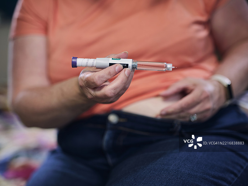 一位女性在家中使用塞马鲁肽笔准备减肥注射剂量，笔中可以装载萨克森达（利拉鲁肽）或维戈维（塞马鲁肽）。这位女性展现了现代、积极的个人健康管理方式。图片素材
