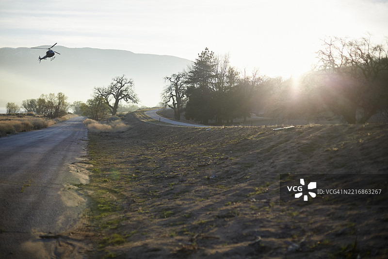 直升机飞越一条蜿蜒的道路，穿过一片荒凉而阳光明媚的景观。美国洛杉矶图片素材