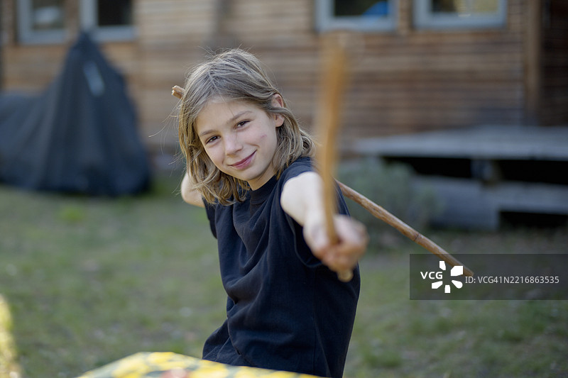 年轻的青少年在户外顽皮地拿着两根棍子，背景是一座木制建筑。德国图片素材