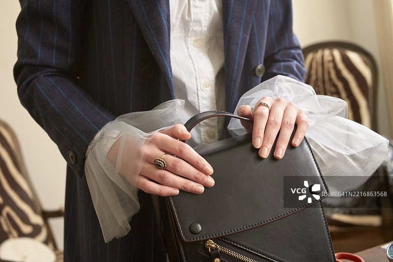身穿蓝色条纹西装的女性在优雅的环境中手持黑色皮革手袋的特写镜头。德国图片素材
