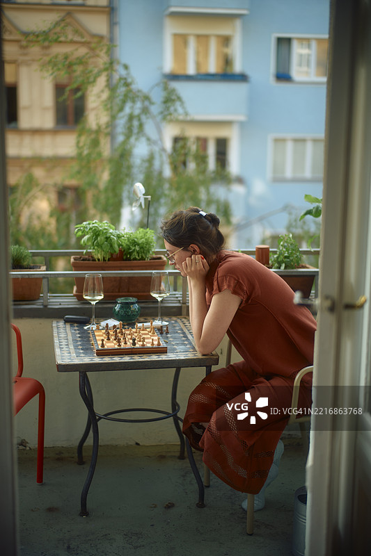 穿着红色连衣裙的女人在城市阳台上独自下棋图片素材