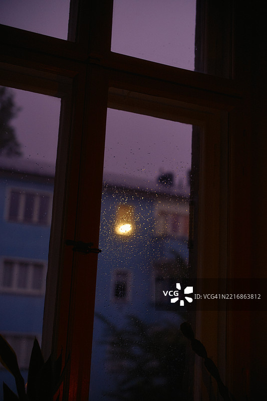 雨点洒落的窗户，黄昏时分可以看到一座蓝色建筑图片素材