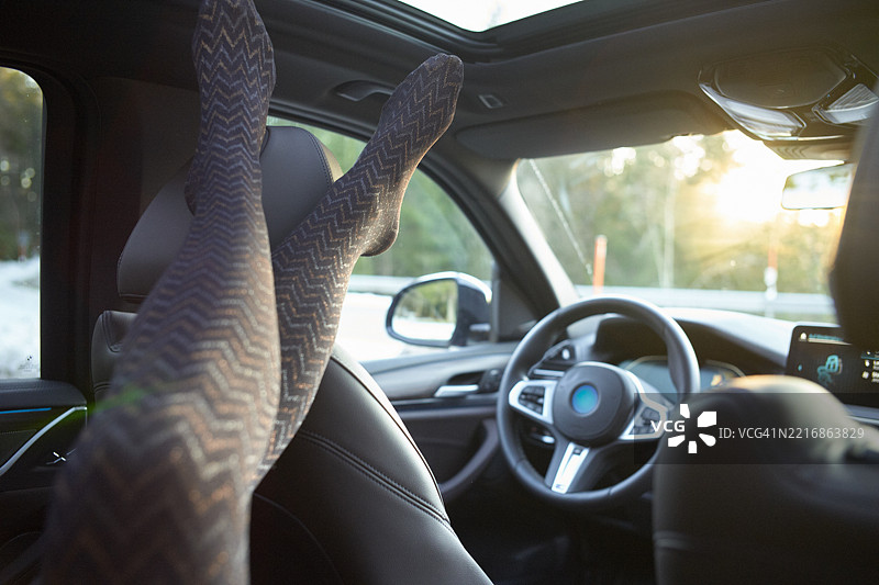 穿着图案紧身裤的腿放在汽车座椅上，阳光照射的车内，方向盘可见图片素材