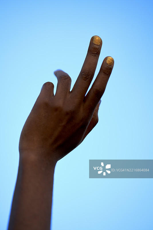 一只涂有金色指甲油的手在晴朗的蓝天背景下。美国纽约市图片素材
