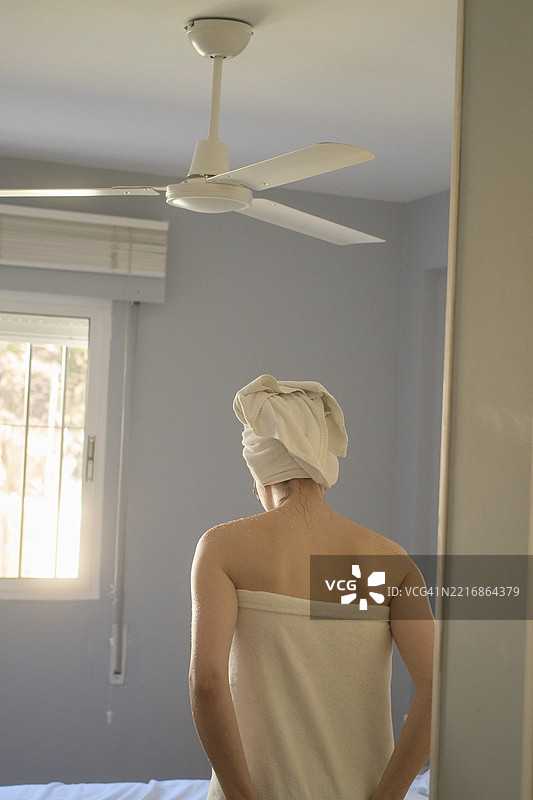 裹着毛巾的女人，头上披着毛巾，凝视着阳光明媚的窗外。西班牙，马拉加图片素材