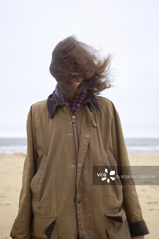 在风吹拂的海滩上，女人的头发被吹得遮住了脸。比利时，奥斯坦德图片素材