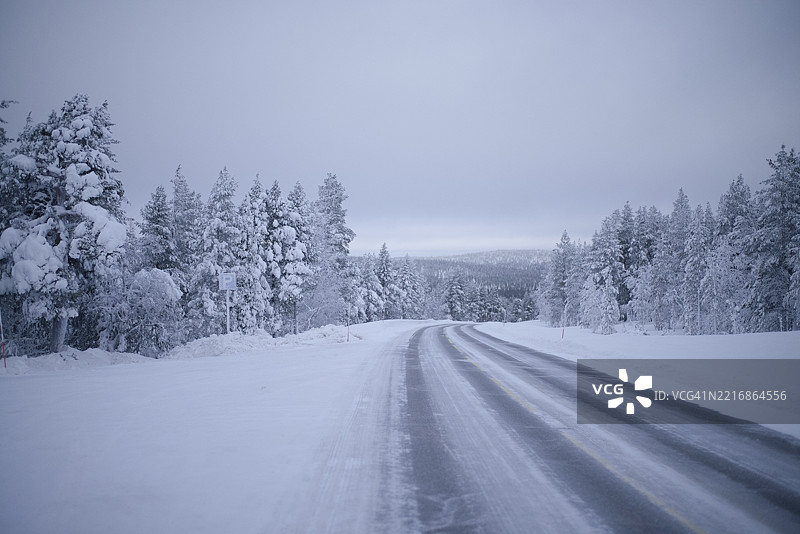 被云层覆盖的天空下，宁静冬季森林中的雪覆盖道路。北芬兰图片素材