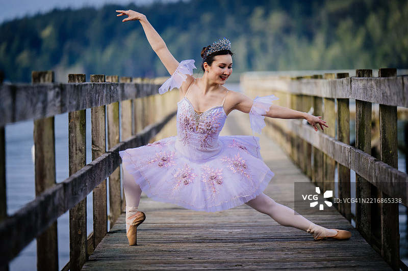 芭蕾舞者在宁静的湖边木栈道上优雅地表演，身穿粉色芭蕾舞裙。华盛顿州，美国图片素材