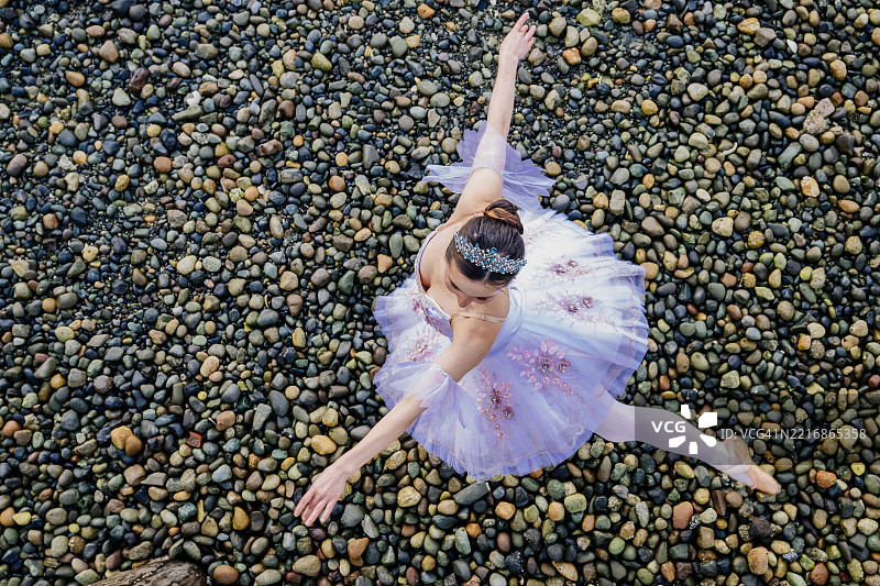 一位穿着芭蕾舞裙的芭蕾舞者在岩石海岸上优雅地摆出一个姿势，从上方俯视。华盛顿州，美国图片素材