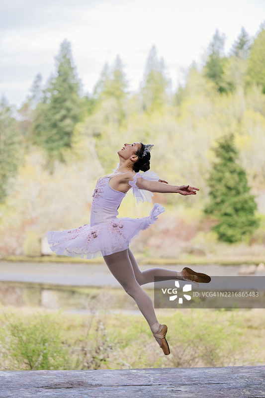 穿着粉色芭蕾舞裙的芭蕾舞者在郁郁葱葱的森林背景下优雅地跳跃。华盛顿州，美国图片素材