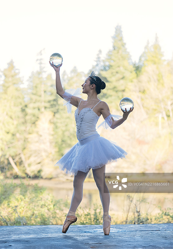 穿着薰衣草色芭蕾舞裙的芭蕾舞者在户外优雅地踮起脚尖，手中托着水晶球。华盛顿州，美国图片素材