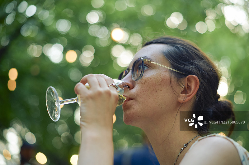 戴着眼镜的女人在户外品酒，周围环绕着虚化的灯光图片素材