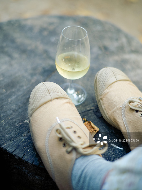 米色运动鞋放在石质表面上，旁边有一杯白葡萄酒。图片素材