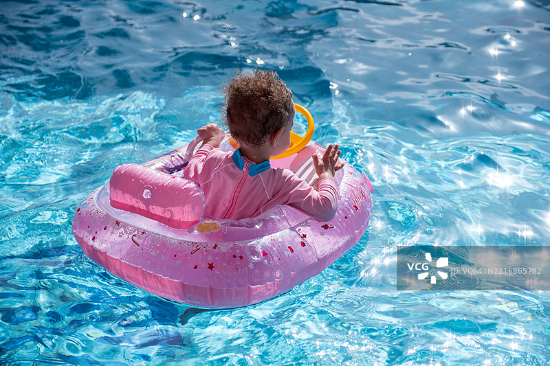 微笑的孩子在夏日阳光下享受游泳池时光，手里拿着粉色浮筒图片素材