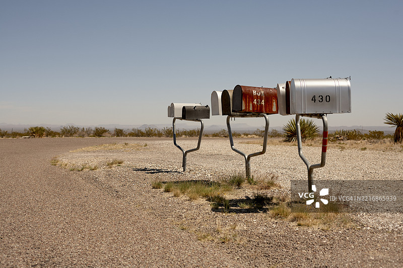 沙漠风景中有三个乡村邮箱，靠近一条蜿蜒的碎石路。美国公路旅行图片素材