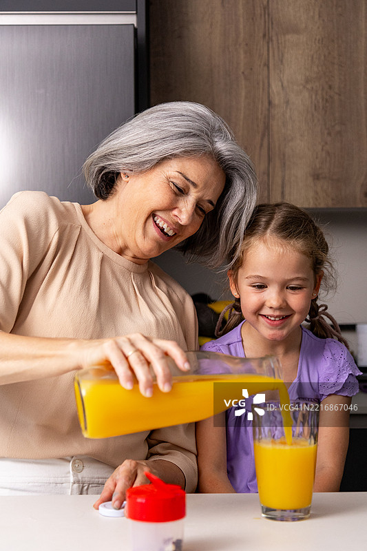 祖母在厨房为孙女倒橙汁图片素材